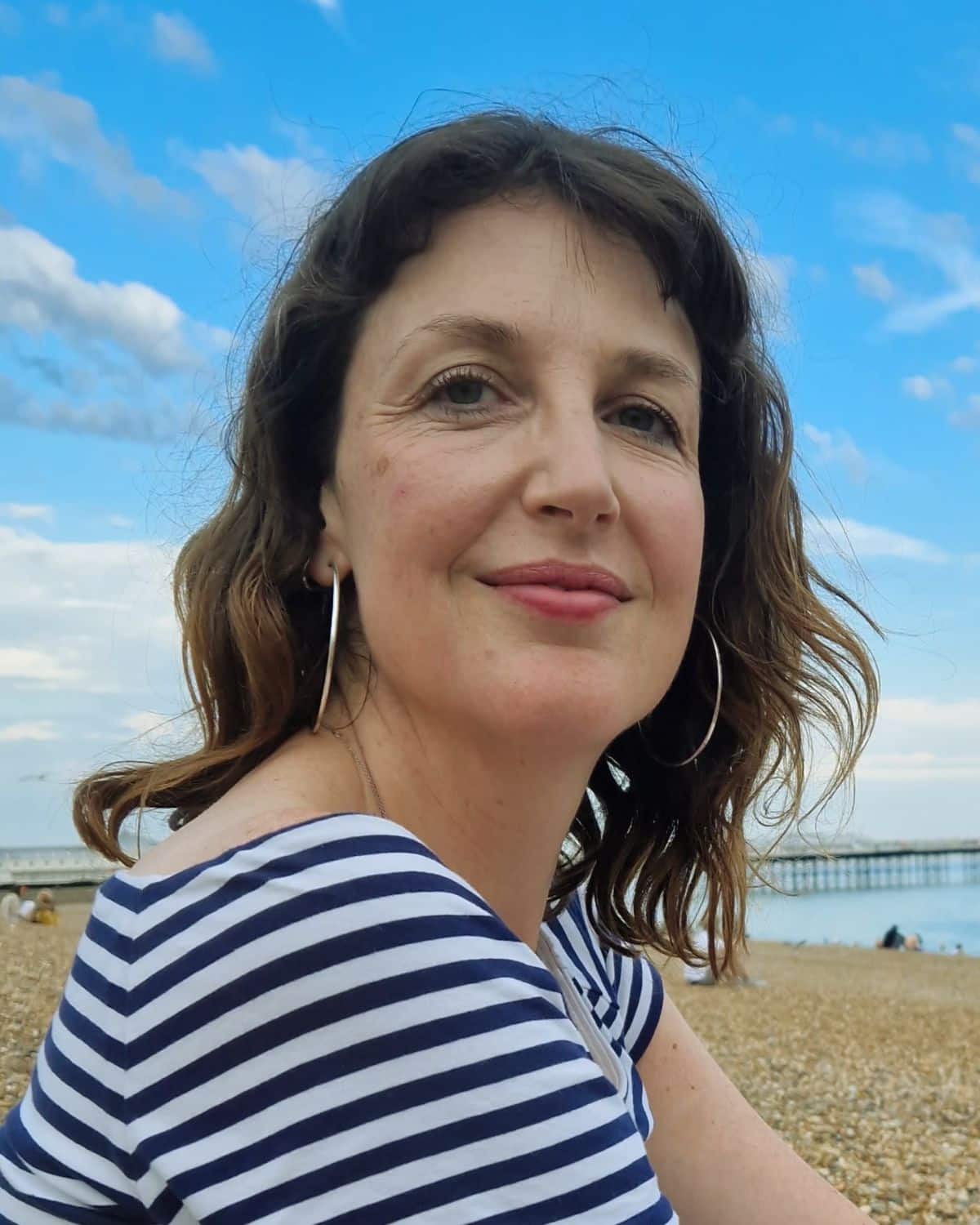 Amy Hutson, counsellor, supervisor and trainer, on the seafront with a pier behind her.
